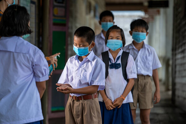 Учитель носит защитную маску для защиты от Ковид-19 и лечит руки учеников антисептиком в классе, начальной школе, обучении и концепции людей.