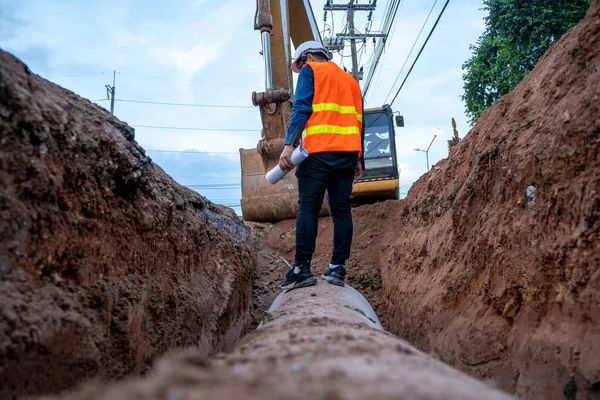Mühendis güvenlik üniforması giyerek inşaat alanındaki beton drenaj borusunu ve rögar su sistemini inceliyor..