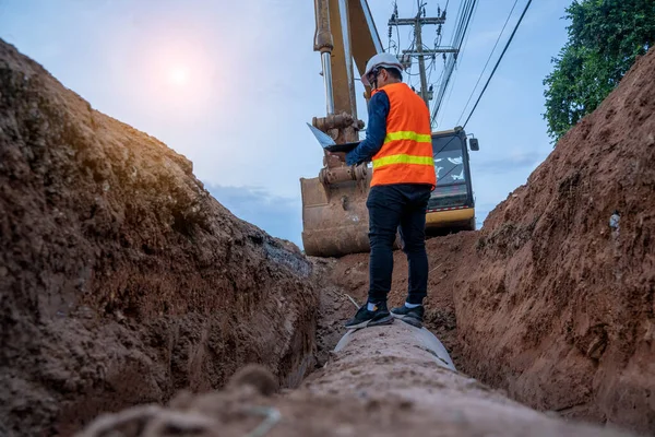 Mühendis güvenlik üniforması giyerek inşaat alanındaki beton drenaj borusunu ve rögar su sistemini inceliyor..