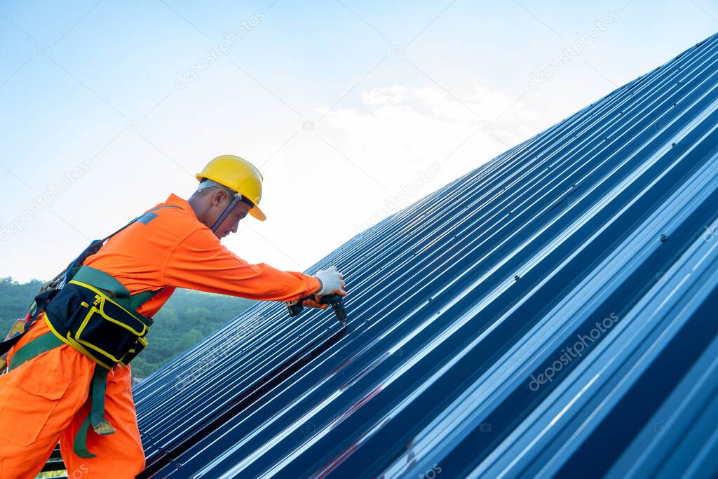 Close up photo of Professional and qualified roofer in protective uniform wear use electric drill to install the metal sheet on the new roof at construction site.