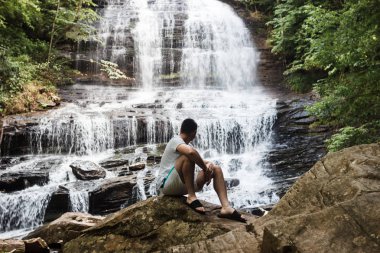 Genç bir adam şelaleye bakıyor. Ormanda turist şelaleye bakıyor. Yaz aylarında orman arasında güzel yüksek şelale. Şelale ve botanik koruma Pearson Falls, Saluda, NC, ABD