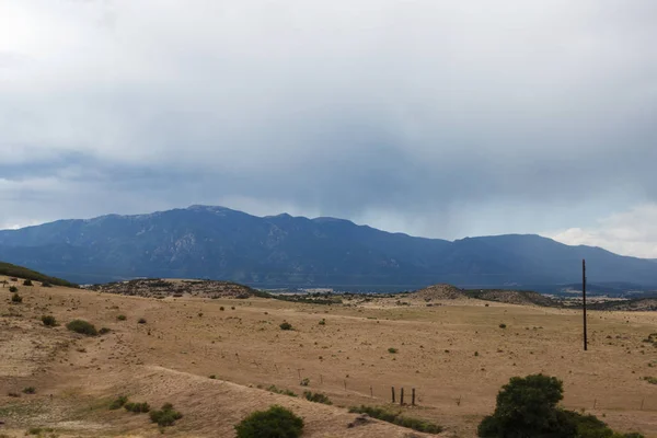 Mountain summer landscape with dark cloudy sky and land with dry grass. In the mountains before the storm. There are pillars with strained wires for electricity.