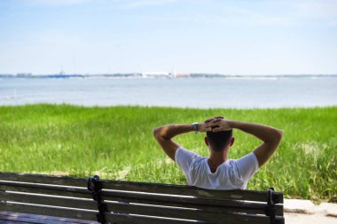 Genç bir adam parkta bir bankta oturur ve okyanusa benziyor. Genç adam parkta bankta dinleniyor.