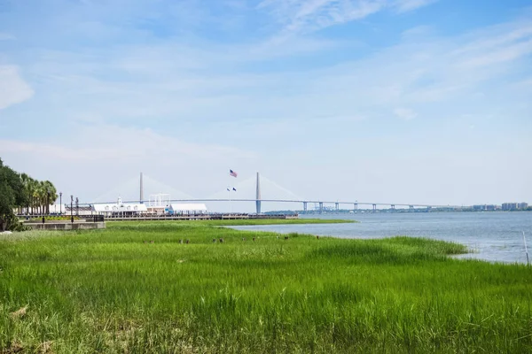Beautiful summer landscape with green grass in the foreground, a bridge in the center and a clear blue sky. The famous bridge in the city of Charleston. Charleston,South Carolina / USA - July 21, 2018