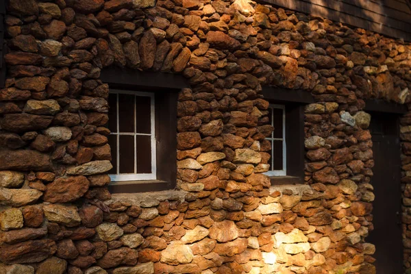 The wall of stone walls with windows illuminated by the sun. Wall of an old stone house with windows and a door