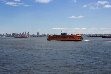 Turuncu bir gemi insanları New Jersey'deki adalara götürüyor. Mesafenin arka planında New York, Manhattan'ın gökdelenleri var..