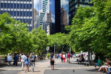 İnsanlar bir yaz günü gökdelenler ve ağaçlar arasında yürürler. New York meydanında, turistler yüksek teknoloji tarzı ağaçlar ve yüksek binalar arasında yürüyor. Manhattan, New York.