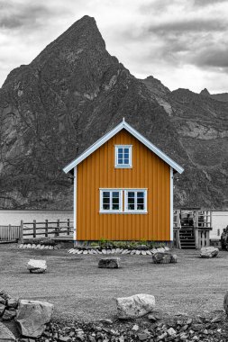 A traditional Norwegian rorbu, a fisherman's cabin, stands proudly against the backdrop of a dramatic mountain range and the sea. These cabins are often used as seasonal homes for fishermen and tourists alike, offering a unique and picturesque experi