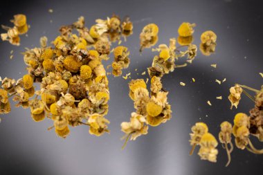 Koyu bir yüzeyde sarı merkezli kurumuş papatya çiçekleri ve soluk yapraklar, bitki çayını, rahatlamayı, doğal çareleri ve yatıştırıcı sağlık faydalarını sembolize ediyor..