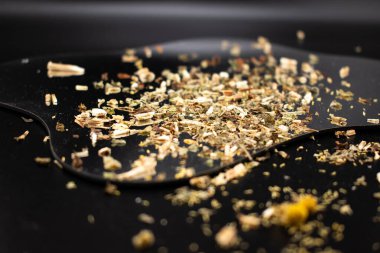 Koyu bir yüzeyde, kurumuş yaprakları ve kökleri toprak tonlarında gösteren, iyiliği, doğal çareleri ve geleneksel çay karışımlarını sembolize eden gevşek yapraklı bitki çayının yakın çekimi..