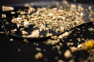 Koyu bir yüzeyde, kurumuş yaprakları ve kökleri toprak tonlarında gösteren, iyiliği, doğal çareleri ve geleneksel çay karışımlarını sembolize eden gevşek yapraklı bitki çayının yakın çekimi..