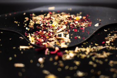 Renkli kurutulmuş bitki çayı, gül yaprakları, papatya çayı ve siyah bir yüzeye saçılmış baharatlar, refahı, doğal sağlığı ve aromatik tadı sembolize eder..