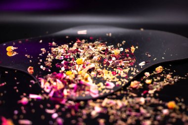 Renkli kurutulmuş bitki çayı, gül yaprakları, papatya çayı ve siyah bir yüzeye saçılmış baharatlar, refahı, doğal sağlığı ve aromatik tadı sembolize eder..