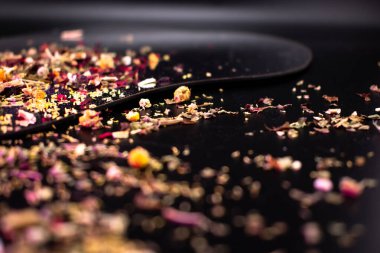 Renkli kurutulmuş bitki çayı, gül yaprakları, papatya çayı ve siyah bir yüzeye saçılmış baharatlar, refahı, doğal sağlığı ve aromatik tadı sembolize eder..