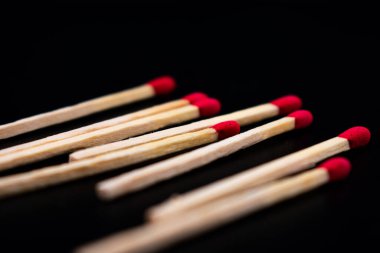 Siyah zemin üzerine dağılmış kırmızı uçlu ahşap kibritlerin yakın plan çekimi, doğal ahşap doku ve çarpıcı başlar arasındaki kontrastı vurguluyor.