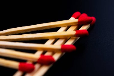 Siyah zemin üzerine dağılmış kırmızı uçlu ahşap kibritlerin yakın plan çekimi, doğal ahşap doku ve çarpıcı başlar arasındaki kontrastı vurguluyor.