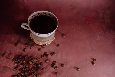 Dağınık fasulyeli bir bardak sade kahve. Sıcak kırmızımsı kahverengi arka plan ve yumuşak ışıklandırma rahatlamak için samimi ve davetkar bir atmosfer yaratır..