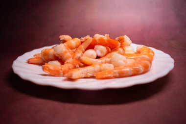 Beyaz deniz tarağı tabağında pembe ve beyaz renkte pişmiş karides. Parlak dokusu tazeliği gösteriyor. Protein açısından zengin deniz ürünleri, küresel mutfaklarda servis ediliyor..