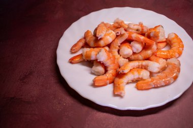 Beyaz deniz tarağı tabağında pembe ve beyaz renkte pişmiş karides. Parlak dokusu tazeliği gösteriyor. Protein açısından zengin deniz ürünleri, küresel mutfaklarda servis ediliyor..