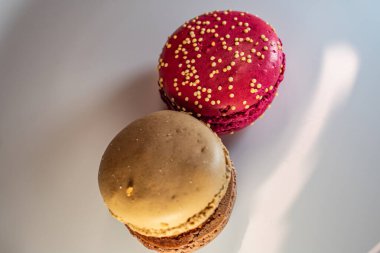 Beyaz çiçek kaplamalı renkli badem kurabiyeleri ve sıcak desenli arka plan. Kırmızı, bej ve çikolata renginde görünür dolgular. Sıcak ve davetkar tatlı natürmort.