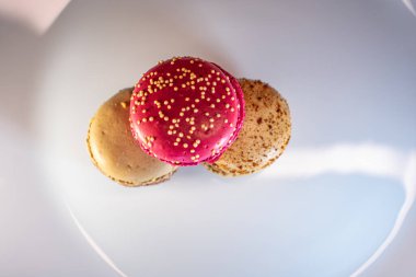 Beyaz çiçek kaplamalı renkli badem kurabiyeleri ve sıcak desenli arka plan. Kırmızı, bej ve çikolata renginde görünür dolgular. Sıcak ve davetkar tatlı natürmort.