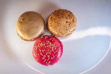 Beyaz çiçek kaplamalı renkli badem kurabiyeleri ve sıcak desenli arka plan. Kırmızı, bej ve çikolata renginde görünür dolgular. Sıcak ve davetkar tatlı natürmort.