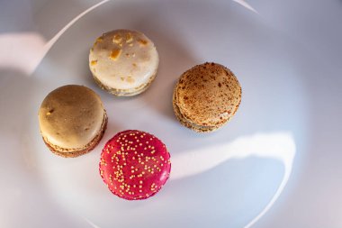 Beyaz çiçek kaplamalı renkli badem kurabiyeleri ve sıcak desenli arka plan. Kırmızı, bej ve çikolata renginde görünür dolgular. Sıcak ve davetkar tatlı natürmort.