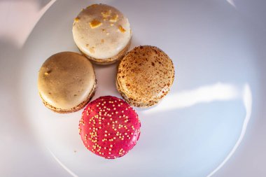 Beyaz çiçek kaplamalı renkli badem kurabiyeleri ve sıcak desenli arka plan. Kırmızı, bej ve çikolata renginde görünür dolgular. Sıcak ve davetkar tatlı natürmort.