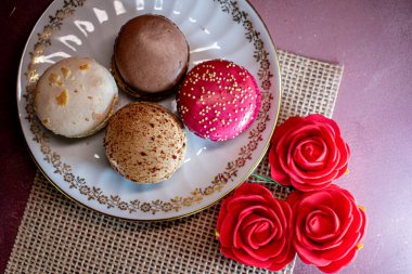 Çuval bezinin üzerindeki beyaz dekoratif tabak renkli badem kurabiyeleri içeriyor, samimi ve davetkar bir ortam yaratıyor. Yumuşak dokular ve ılık tonlar rahatlatıcı bir sabahı ve tatlı bir hoşgörünün zevkini çağrıştırıyor..