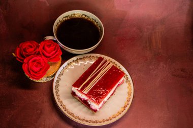 Üzerinde beyaz çikolata parçacıkları olan parlak kırmızı bir tatlı bir fincan koyu kahvenin yanında çiçek tabağında duruyor. Zarif, cezbedici bir sahne zengin aromayı ve tatlı hoşgörü için şenlikli zarafeti harmanlayan.