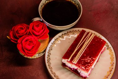 Üzerinde beyaz çikolata parçacıkları olan parlak kırmızı bir tatlı bir fincan koyu kahvenin yanında çiçek tabağında duruyor. Zarif, cezbedici bir sahne zengin aromayı ve tatlı hoşgörü için şenlikli zarafeti harmanlayan.