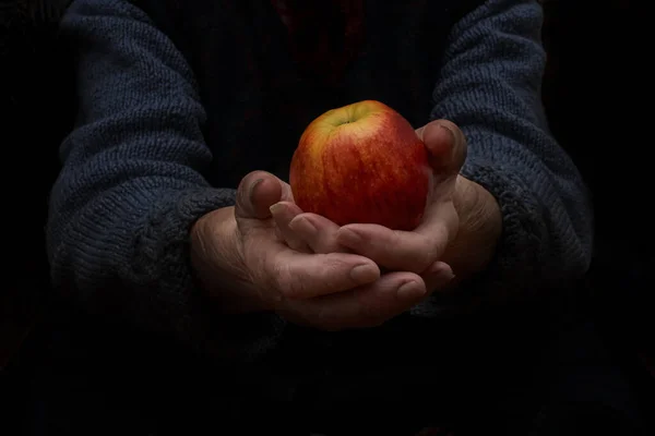 Grandma gives an apple. Grandmother holds an apple in both hands. Low key. Horizontal frame.