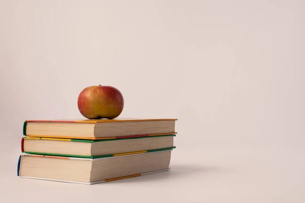 Masanın üzerinde kitaplar var. Kitaplarda kırmızı bir elma var. Vanilyalı tonlama. Yatay çerçeve.