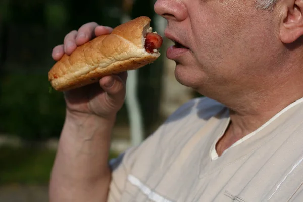 The man is eating a hot dog. The hot dog is tasty, but not healthy. Local focus. Horizontal frame.