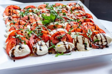 Mozzarella peyniri domates, fesleğen ve balsamik sirke beyaz tabakta düzenlenmiş Caprese salatası
