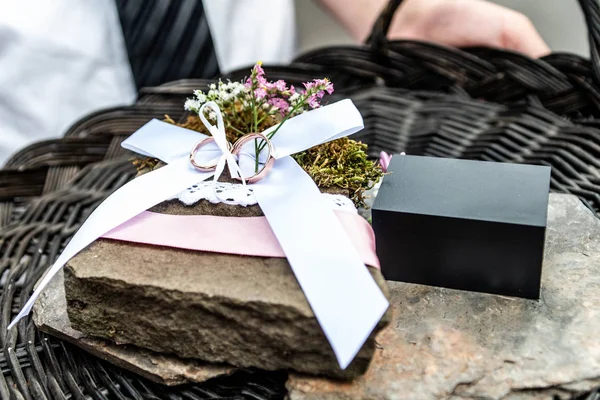 Красивые обручальные кольца лежат на каменной поверхности на фоне букета цветов свадебной пары — стоковое фото