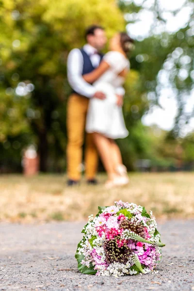 Ramo de bodas en frente de los recién casados fondo de la pareja, besos de profundidad poco profunda bokeh — Foto de Stock