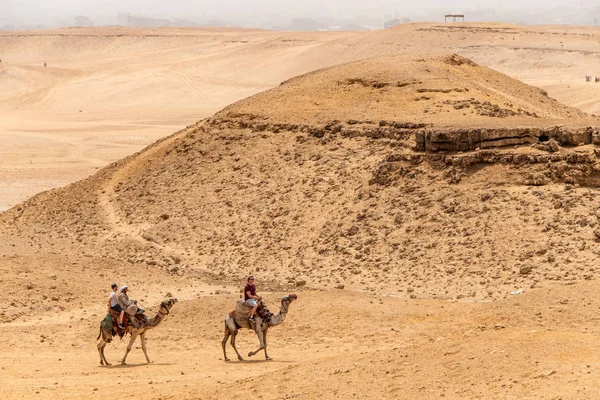 Cairo, Egitto 25.05.2018 - Turisti e guide a cavallo di cammelli sull'altopiano di Giza nel deserto roccioso — Foto Stock