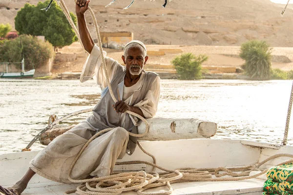 ASWAN, EGIPTO 21.05.2018 Viejo hombre nubio sentado en la cubierta del barco Felucca y navegando por el río Nilo — Foto de Stock