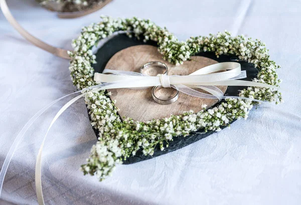 Красивые обручальные кольца лежат на белой поверхности на фоне букета цветов и свадебной пары — стоковое фото