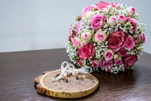 Beautiful wedding rings lie on wooden surface against the background of a bouquet of flowers and wedding couple — Stock Photo, Image