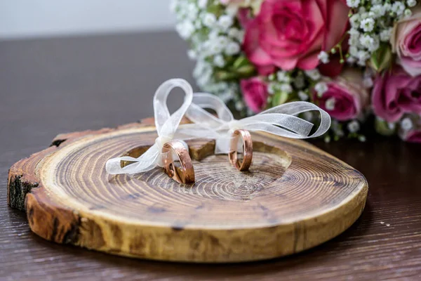 Beautiful wedding rings lie on wooden surface against the background of a bouquet of flowers and wedding couple — Stock Photo, Image