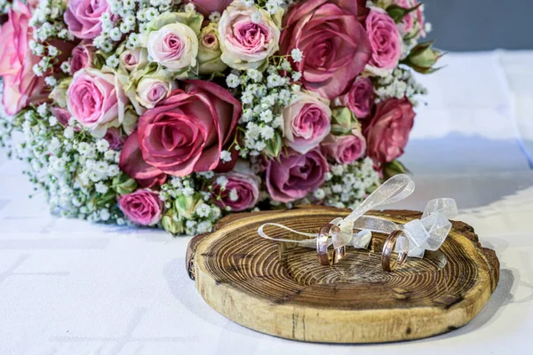 Beautiful wedding rings lie on white surface against the background of a bouquet of flowers and wedding couple — Stock Photo, Image