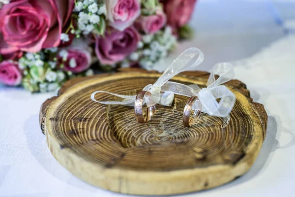 Beautiful wedding rings lie on white surface against the background of a bouquet of flowers and wedding couple — Stock Photo, Image