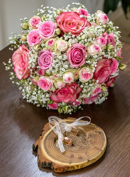 Belos anéis de casamento jazem na superfície de madeira contra o fundo de um buquê de flores e casal de casamento — Fotografia de Stock