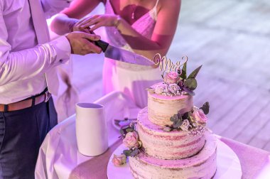 Bir sürü katlı güzel bir düğün pastasını taze çiçekler ve güllerle kesiyor.