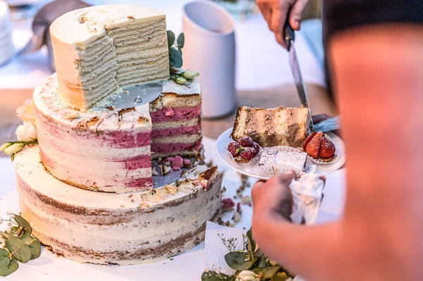 Cortar un delicioso hermoso pastel de boda en muchos niveles con flores silvestres frescas y rosas — Foto de Stock