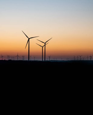 Rüzgâr türbinlerinin siyah silueti enerji jeneratörü Almanya 'da bir rüzgar çiftliğinde gün batımında