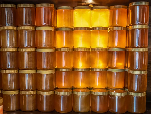 Башня и ряды золотисто-желтого меда в стеклянной банке на деревянной доске — стоковое фото