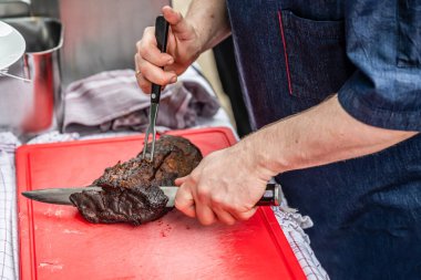 Şef bıçakla kesilmiş sigara içen biri kırmızı kesim tahtasının üzerinde et filetosu tüttürmüş ve BBC Southfood temalı ızgara yapıyor
